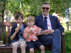 A guest sitting on a bench with his children who are enjoying ice creams.